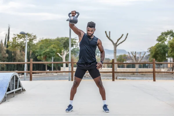 Full body of determined African American male athlete in activewear lifting heavy weight on sports ground during fitness workout