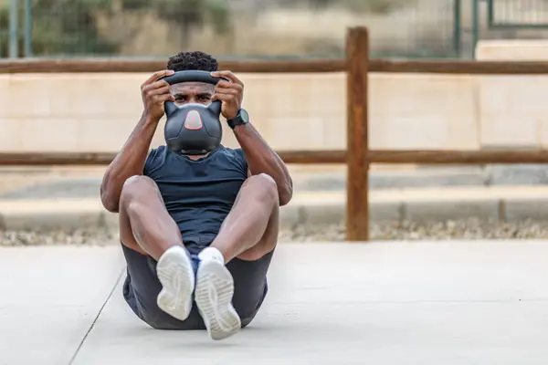 Full body of determined young African American male athlete in sportswear doing abdominal crunches during fitness session on summer day