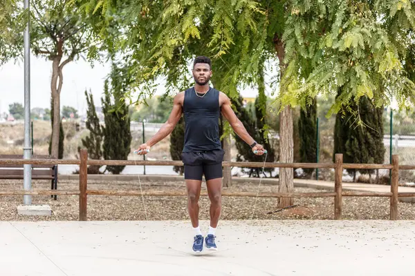 カーディオトレーニング中に夏の公園でロープをジャンプするスポーツ服やスニーカーで決定されたアフリカ系アメリカ人の男性アスリートの全身 ストック写真