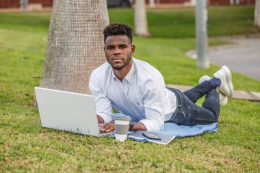 Bir Afro-Amerikalı çimlerin üzerinde çalışırken ya da çalışırken dizüstü bilgisayar kullanıyor..