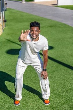 30 'lu yaşlarında Afro-Amerikan kökenli bir adam halka açık bir parktaki canlı yeşil bir arazide duruyor..