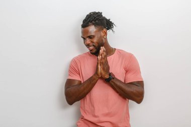 Saçları örgülü bir adam ellerini birleştirip gülümseyerek şükran ya da dua eder. Sıradan pembe bir gömlek giyer ve sıcak, pozitif bir enerji yayar. Basit, beyaz bir arka plana karşı hafif bir atmosfer yaratır..