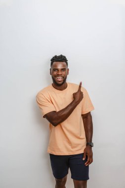 Neşeli, kıvırcık saçlı, Afro-Amerikan bir adam parmağını yukarı kaldırırken kendinden emin bir şekilde gülümsüyor. Açık şeftali rengi bir gömlek giymiş ve parlak bir iç mekanda arkasında da renkli bir duvar var..