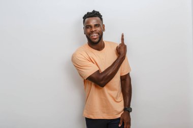 Kıvırcık saçlı neşeli bir adam yukarı işaret ederken kendine güvenerek gülümsüyor. Açık şeftali rengi bir gömlek giyiyordu ve arkasında tarafsız bir duvar bulunan parlak bir iç mekâna yerleştirildi..