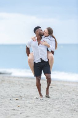 Bir çift Zapillo sahilinde, Almeria, İspanya 'da, adamın sırtında, kumlu sahil boyunca at sürerken keyifli bir anı paylaşıyor. Güneş, onlar kucaklaşırken ve gülümserken parlıyor, sakin denizle olan ilişkilerinin sıcaklığını bir perde gibi özetliyor..