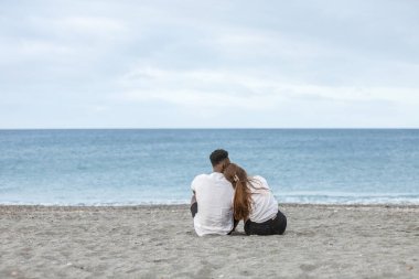 Playa del Zapillo, Almerya, İspanya 'nın kumlu sahillerinde bir çift yan yana oturur. Samimi bir anı paylaşıyorlar, bulutlu gökyüzü dinlenme günleri için sakin bir zemin hazırlarken sakin, mavi denize bakıyorlar..