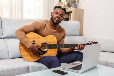 Bir müzisyen, rahat bir yaşam ortamı ile çevrili olan akustik gitarını tıngırdatırken derinden odaklanır. Yanında dizüstü bilgisayarı ve telefonu olan bir kanepede oturup müzik seansının keyfini çıkarıyor..