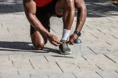 33 yaşındaki Afro-Amerikalı bir adam halka açık bir parkta spor faaliyetlerine hazırlanıyor. Diz çöker, bağcıklarını bağlar, dışarıda eğlenirken fiziksel egzersize hazırlanır..