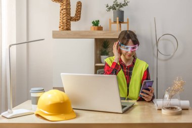 Güvenlik yeleği giyen kadın gelişmiş yapay zeka gözlüğü takarken akıllı telefonuyla meşgul..