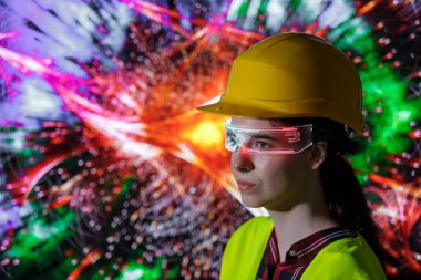 Sert şapka ve güvenlik yeleği giyen bir kadın renkli ve soyut dijital bir görüntüyü izlerken yapay zeka gözlüğü kullanır..