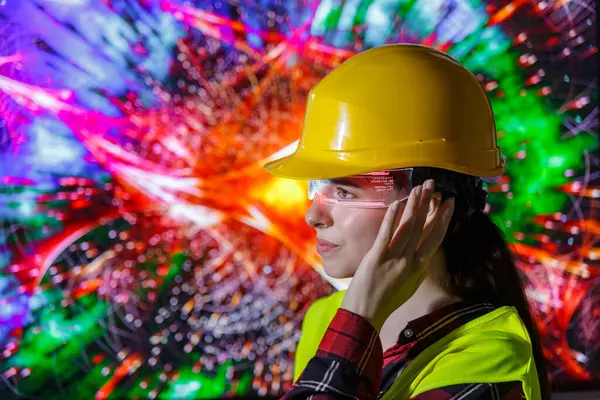 Sarı şapka ve güvenlik yeleği giyen genç bir bayan işçi gelecekteki yapay zeka gözlükleriyle etkileşime geçiyor..