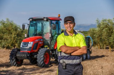 Güvenlik elbiseli bir adam Endülüs 'te bir zeytinlikte traktörün önünde duruyor..
