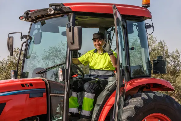Neşeli bir çiftçi parlak kırmızı bir traktörün sürücü koltuğunda otururken kamerayı selamlar. Zeytin koruluğu traktörü çevreleyerek canlı bir tarım ortamı sergiliyor..