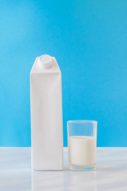 Boş etiketli süt kutusu ve mavi arka plan ambalajında bir bardak süt.