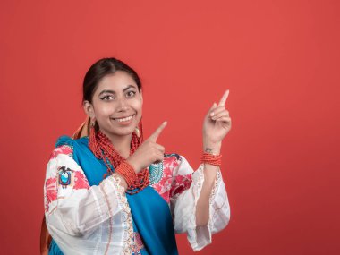 beautiful latina girl wearing an ecuadorian indian costume on red background pointing with her fingers to her left side clipart