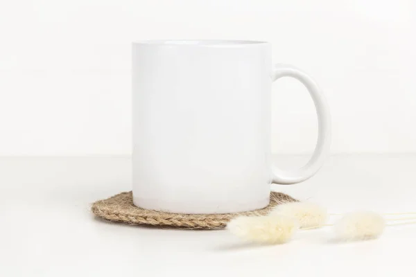 Kenevir altlığı, kurutulmuş çiçekler ve doğal renkte beyaz kupanın masayı. Boş kahve fincanı Boho stilinde taklit edilir..