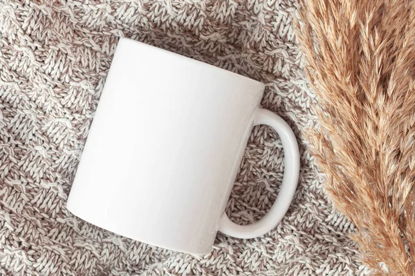 Mockup of white mug on knitted plaid with dried flowers, in neutral beige color. Blank coffee cup mug mock up in Boho style, flat lay.