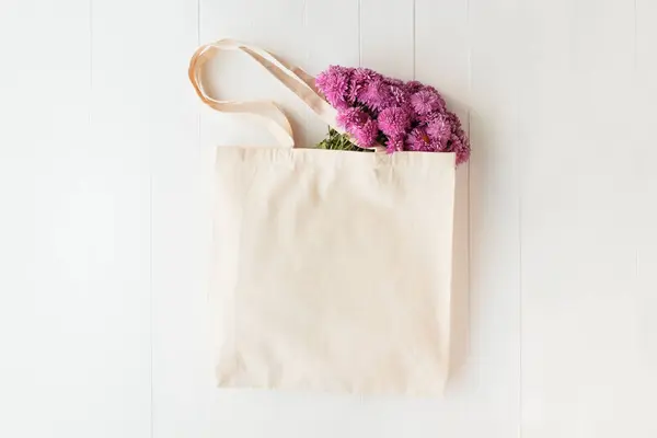 Tote bag mockup. Canvas bag with pink flowers lies on white wooden table. Eco shopping bag with copy space.