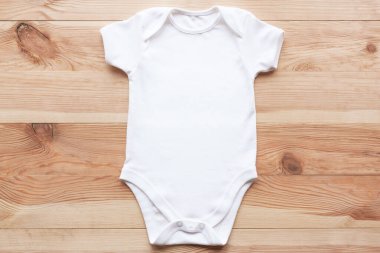 Tahta arka planda beyaz bebek tulumu modeli. Boş bebek kıyafetleri şablonu, düz yatış.
