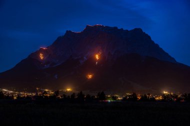 Traditional mountain bonfires for the summer solstice in the Tiroler Zugspitz Arena around the Ehrwald Lermoos Biberwier basin clipart