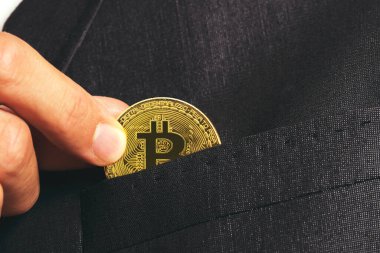 İzmir, Türkiye - 11 Ağustos 2022: İşadamı Eli takım elbisenin cebine koymak için bir bitcoin tutuyor.