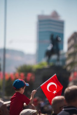 İzmir, Türkiye - 9 Eylül 2022: Türkiye Cumhuriyeti 'nin Konak Alsancak Meydanı' nda İzmir gününde, yetişkin birinin omuzlarında Türk bayrağı ve tişörtü taşıyan bir çocuk.