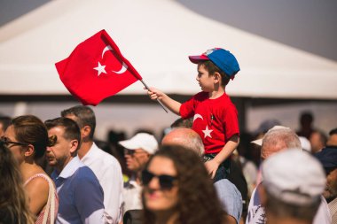 İzmir, Türkiye - 9 Eylül 2022: Türkiye Cumhuriyeti 'nin Konak Alsancak Meydanı' nda İzmir gününde, yetişkin birinin omuzlarında Türk bayrağı ve tişörtü taşıyan bir çocuk.