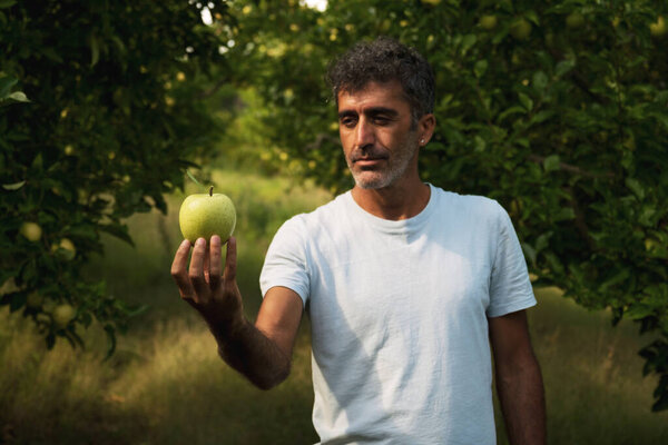 Portrait of a middle eastern holding an apple in his hand and posing in an apple orchard