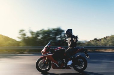 Side view of a motorcycle rider riding red race motorcycle on the highway with no hands and with motion blur.  clipart