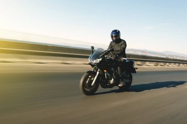 Hareket bulanıklığı olan bir arka planda motosiklet süren motosiklet sürücüsünün yan görüntüsü