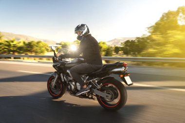 Hareket bulanıklığıyla yolda giden bir motorcunun yan görüntüsü. 