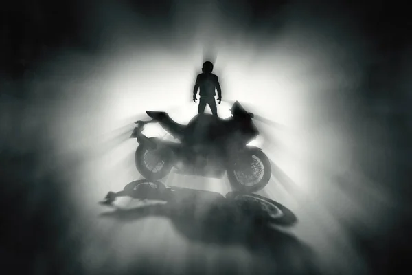 Silhouette of a motorcycle rider with a helmet and defocused race motorcycle with fog on a dark background.