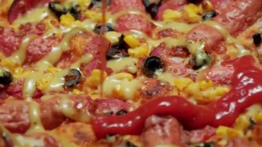 Sosis, zeytin, peynir, ballı hardal ve dökülen ketçapla dönen sıcak pizzanın görüntülerini kapat..