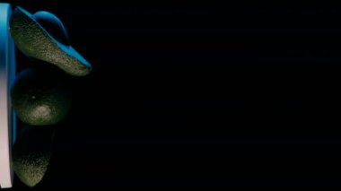 Kesilmiş ve dönen Avokadoların dikey görüntüleri mavi arka planda siyah bir zemin üzerinde.