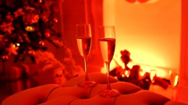 Şöminenin önünde şampanya dolu iki şampanya bardağının, Noel süslerinin ve havai fişeklerin görüntülerini kapat.