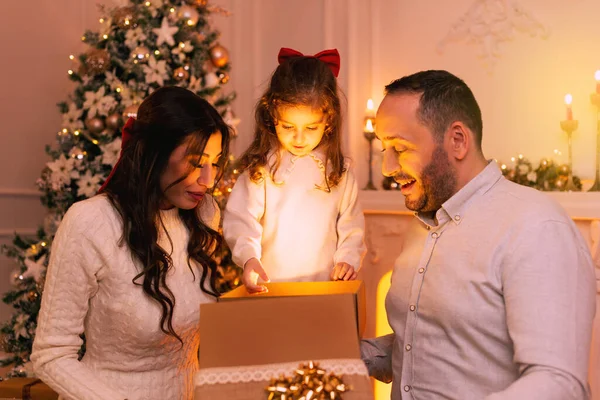 Happy family with surprising emotion while opening a gift box there is a christmas tree, fireplace and candles on the background.