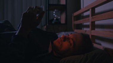 30 'lu yaşlarda erkek, telefonuna ve muhtemelen sosyal medyaya bakıyor ve geceleri yatakta uyuyamıyor..