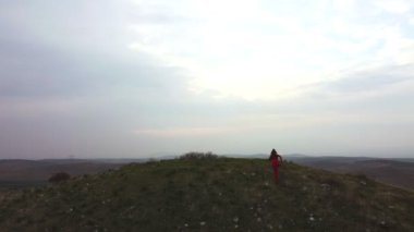Silhouette of a woman in yoga clothes red colored, successfully raising arms on top of a hill on a cloudy background.