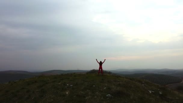ヨガの服の赤い色の女性のシルエット 曇りの背景に丘の上に腕を上げる成功 — ストック動画