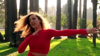 30s one woman with red tights and tops dancing at a public park on green grass with trees on the background