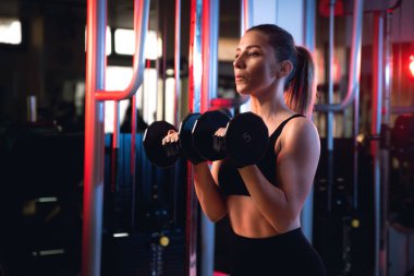 Portrait of a woman doing shoulder press with dumbells in a gym.