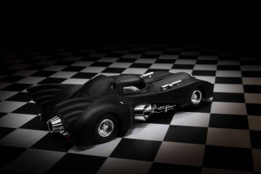 Izmir, Turkey - March 15, 2023: 1989 Batmobile toy model car on a chequered ground and black background. clipart