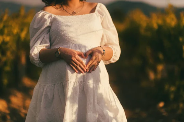 Zbliżenie Kobiety Ciąży Białej Sukience Kształtującej Serce Brzuchu Pośród Winnicy — Zdjęcie stockowe