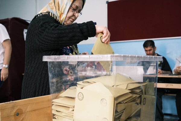 Измир, Турция - 14 мая 2023 года: пожилая женщина, около 60-70 лет, попадает в плен в момент голосования на президентских и парламентских выборах в Турции. Женщина, носящая головной платок, бросает свой бюллетень в транспарант