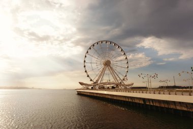 Bakü, Azerbaycan - 28 Haziran 2023: Bakü 'nün Dönme dolabının büyüleyici bir fotoğrafı hafif bulutlu bir gökyüzü altında, sabah güneşinin ılık renkleriyle bezenmiş. 