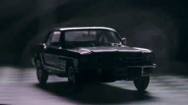 İzmir, Türkiye - 13 Mart 2023: Klasik siyah Ford Mustang 260 'ın gizemli bir sisle kaplandığını gösteren görsel olarak çarpıcı bir video. Araç, siyah arka planda kareli bir zeminde, olay yerine derinlik ve entrika ekliyor..