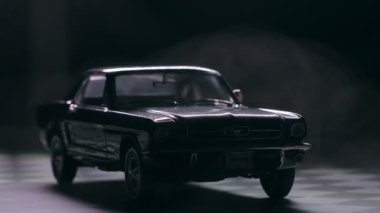 İzmir, Türkiye - 13 Mart 2023: Klasik siyah Ford Mustang 260 'ın gizemli bir sisle kaplandığını gösteren görsel olarak çarpıcı bir video. Araç, siyah arka planda kareli bir zeminde, olay yerine derinlik ve entrika ekliyor..