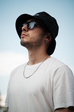 Güneş gözlüklerine yansıyan, 20 'li yaşlarda ciddi bir adamın yakın plan portresi. Açık gökyüzünün arka planı bakışlarının yoğunluğunu arttırıyor.