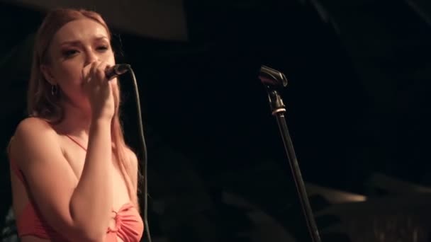 这是一个特写 沉默的视频 描写了一位20多岁的漂亮年轻女子 身穿橙色连衣裙 在舞台上热烈地歌唱 在朦胧的背景下可以瞥见吉他手 — 图库视频影像