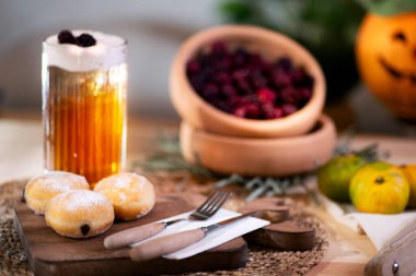 Kesme tahtasında çatal bıçaklı çikolatalı kurabiye, köpüklü elma suyu, kırmızı böğürtlen, mandalina ve arka planda bir Jack O 'Lantern ile servis edilir..